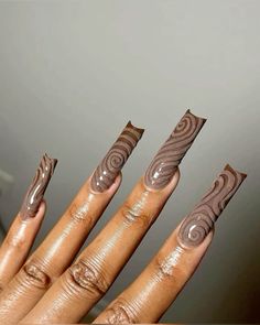 a woman's hand with brown nail polish and swirl designs on her nails, in front of a gray wall