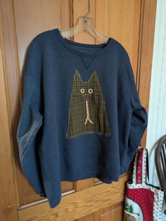 a sweater with an image of a cat on it hanging from a hook in front of a wooden door