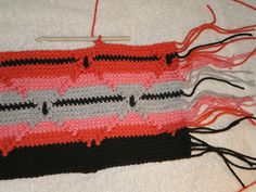 a crocheted red and black piece of cloth on top of a white blanket