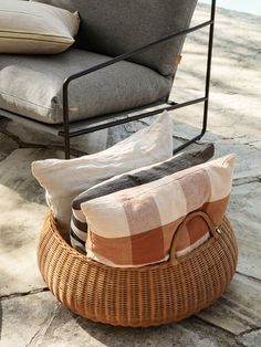 a wicker basket filled with pillows sitting on top of a stone floor next to a chair