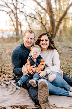 a man, woman and baby are sitting on a blanket in the woods with leaves