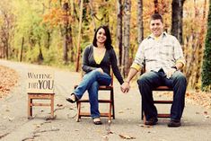 a man and woman sitting on wooden chairs in the middle of an autumn forest holding hands