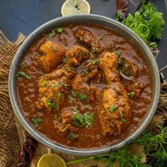 a pan filled with chicken curry and garnished with cilantro, parsley and lemon wedges