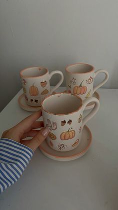 a hand is holding a coffee cup and saucer with pumpkins on the cups