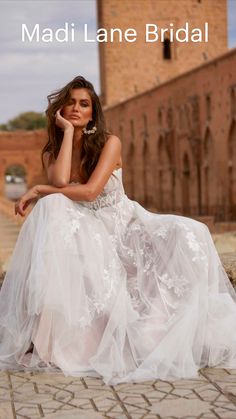 a woman in a white dress sitting on a stone wall next to a brick building