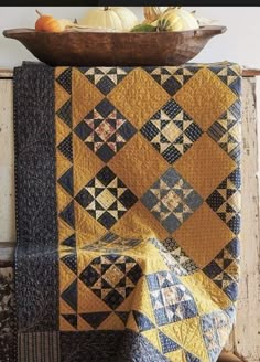 a quilted table runner with pumpkins in the background and an old wooden bowl on top