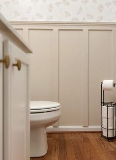 a white toilet sitting in a bathroom next to a wooden floor and wall with flowers on it