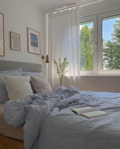 white bedroom, two square blue pillows on simple double sized bed, with two smaller white pillows infront of them, and then a matching light blue blanket over the white mattress. there is a small window beside the bed, in which you can see a blue sky and two large trees. on the wall over the bed are 3 small frames with paintings, and a golden light fixture beside the bed. a vase holding wildflowers is on the side of the bed closest to the window. Baby Blue Bedroom, Vision Board Wall, Classy Interior Design, Simple Dorm Room, Bedding Simple, Dorm Room Colors, Aura Quotes, Redecorate Bedroom, Minimalist Room