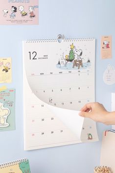 a person holding up a calendar next to a wall with pictures and magnets on it