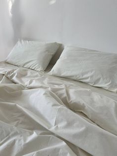 an unmade bed with white sheets and pillows