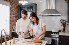 a man and woman standing in a kitchen preparing food on top of a cutting board