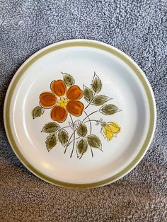 a white plate with orange and yellow flowers painted on the side, sitting on a gray surface