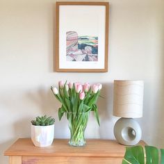 pink tulips in a glass vase on a dresser next to a framed painting