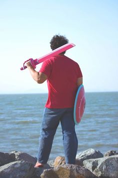 a man holding a pink surfboard on top of a rocky beach next to the ocean