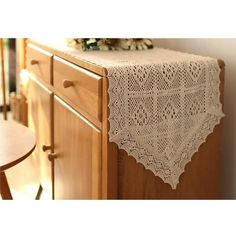 a crocheted table runner on top of a wooden dresser with flowers in the background