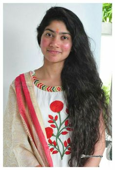 a woman with long black hair wearing a white blouse and pink sari is smiling at the camera