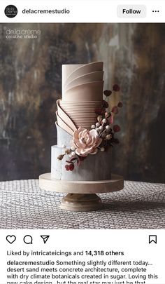 a three tiered cake decorated with flowers and feathers on a wooden stand in front of a wall