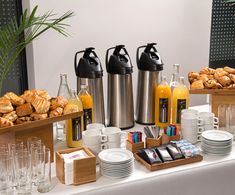 a table topped with plates and cups filled with breakfast foods next to breads, juices and croissants