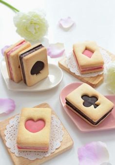 small cakes with hearts on them are sitting on plates next to pink flowers and petals