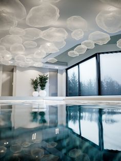 an indoor swimming pool with clear water and bubbles hanging from the ceiling above it, next to a large window