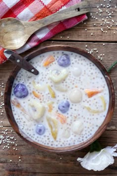 a wooden bowl filled with fruit and yogurt on top of a table next to a spoon