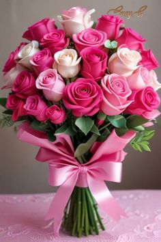 a bouquet of pink and white roses in a vase with a bow on a table