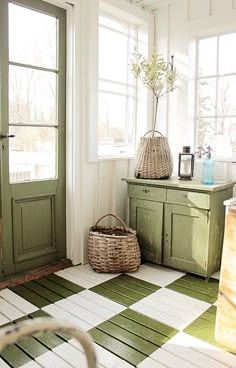 a kitchen with green cabinets and white flooring next to an open door that leads to the outside