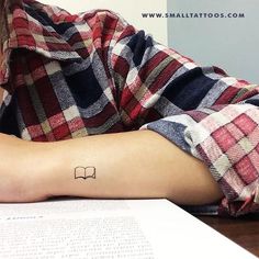 a person with a tattoo on their arm sitting at a table in front of an open book