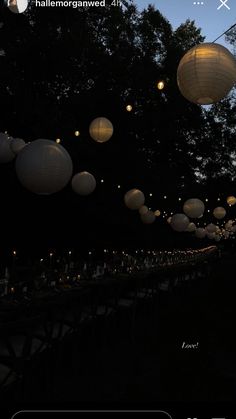 many paper lanterns are lit up in the night sky at an outdoor dinner table with long tables and chairs