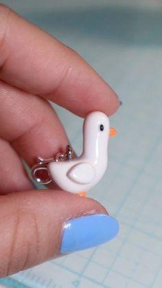 a person holding a tiny white bird keychain in their hand with blue nail polish