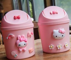 two pink hello kitty containers sitting on top of a wooden table next to each other