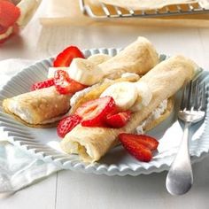 two crepes with strawberries and cream on a plate next to a fork