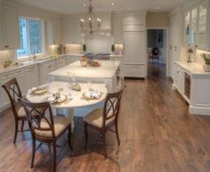 a large kitchen with white cabinets and wooden flooring, along with a dining table set for four