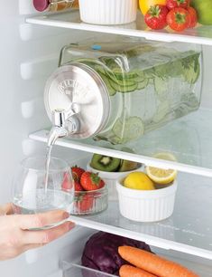 a person is holding a glass in front of an open refrigerator filled with fruits and vegetables