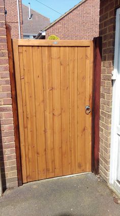 a wooden gate in front of a brick building with a white door on the side