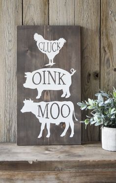 a wooden sign that says cluck and drink moo on it next to a potted plant