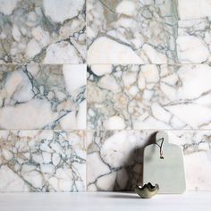 a marble tile wall with a white handle on the left side and a gray ceramic hook on the right side