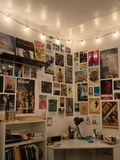 there are many posters on the wall in this dorm room that is decorated with string lights