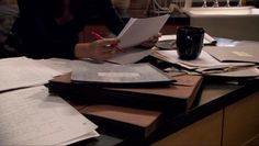 a person sitting at a desk with papers and pens in front of them on top of a table