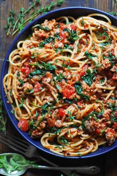 pasta with meat, tomatoes and herbs in a blue bowl on a wooden table next to silverware