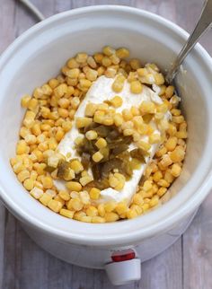 a white bowl filled with corn and cream on top of a wooden table next to a spoon