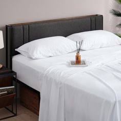 a bed with white sheets and pillows in a bedroom next to a plant on the nightstand