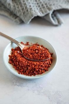 a white bowl filled with red spices next to a gray towel on top of a table