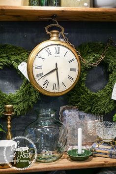 there is a clock that is on the shelf next to other items and glassware