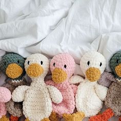 four crocheted stuffed ducks are lined up in a row on a white sheet