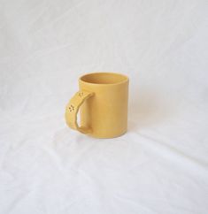 a yellow coffee cup with a handle on a white tableclothed background is shown