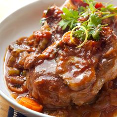 a white plate topped with meat covered in sauce and garnished with parsley