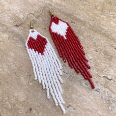 two red and white seed beaded earrings hanging from gold hooks on a stone surface