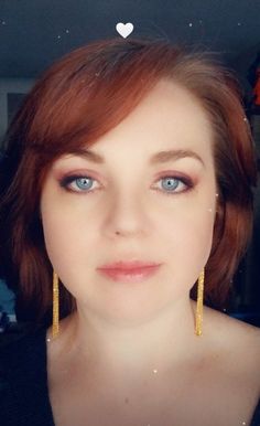 a woman with red hair and blue eyes is wearing gold earrings, looking at the camera