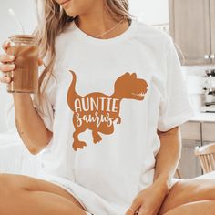 Unleash your inner Auntie Saurus with this fun and quirky shirt! Featuring a playful T-Rex design and the punny phrase "Auntie Saurus," it's perfect for the aunt who loves dinosaurs and embraces her playful side. This comfy and stylish tee is sure to be a hit at family gatherings and a great conversation starter. Auntie Shirts, New Aunt, At Family, Aunt Shirts, Great Conversation Starters, Niece And Nephew, Family Gatherings, T Rex, Dinosaurs